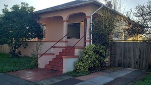 Una casa de un piso con una escalera roja que lleva a la puerta principal, rodeada por una valla de madera y vegetación.