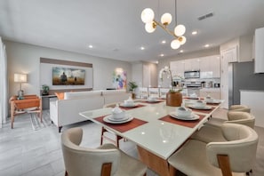 A modern kitchen with white cabinets, a central island, and a dining area with a long table and chairs. - Luxury Modern Decor Best Location Private Pool (Kissimmee)