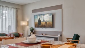 Quarto de hotel moderno com área de refeições, TV de tela plana na parede e vista para um campo pela janela.