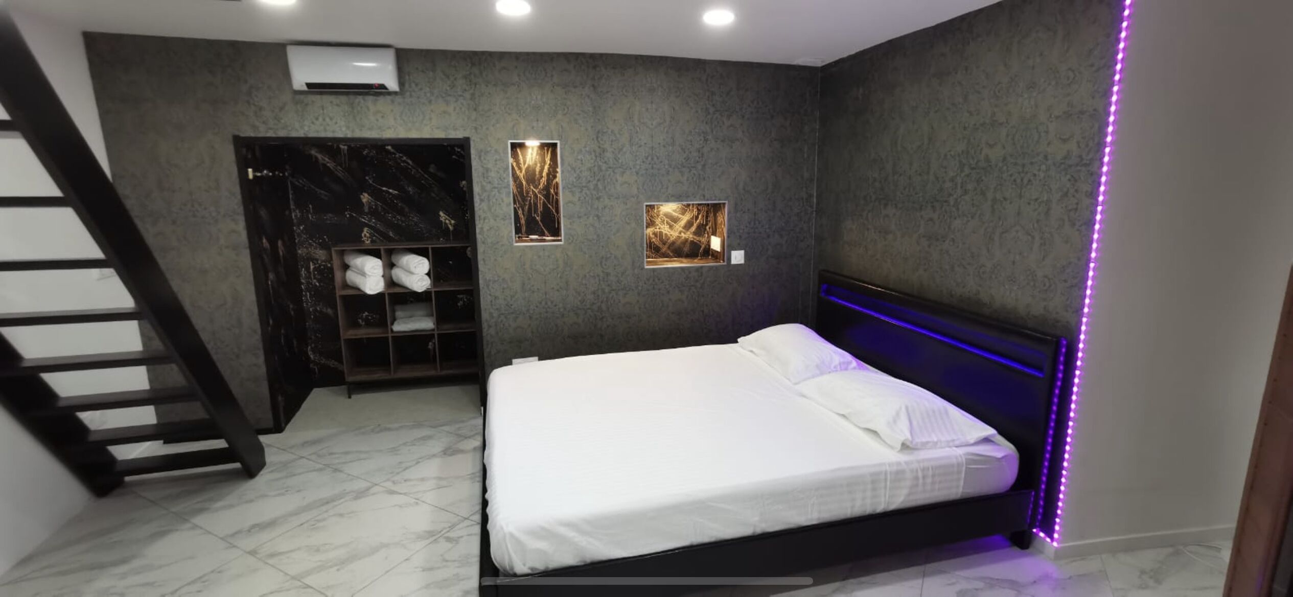 Un dormitorio moderno con cama, armario empotrado, estante con toallas y una escalera.