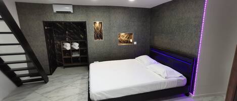 Un dormitorio moderno con cama, armario empotrado, estante con toallas y una escalera.