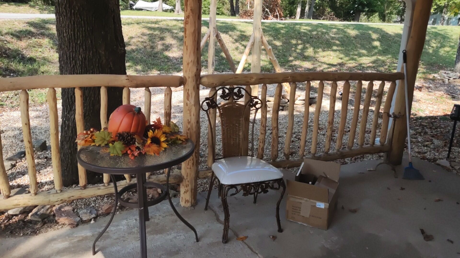 A wooden deck with a metal chair and table, a pumpkin decoration, and a cardboard box on the ground.