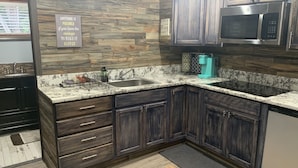A kitchen with dark wooden cabinets, a granite countertop, a stainless steel microwave, and a coffee maker. - Cedar house (Rockaway Beach)