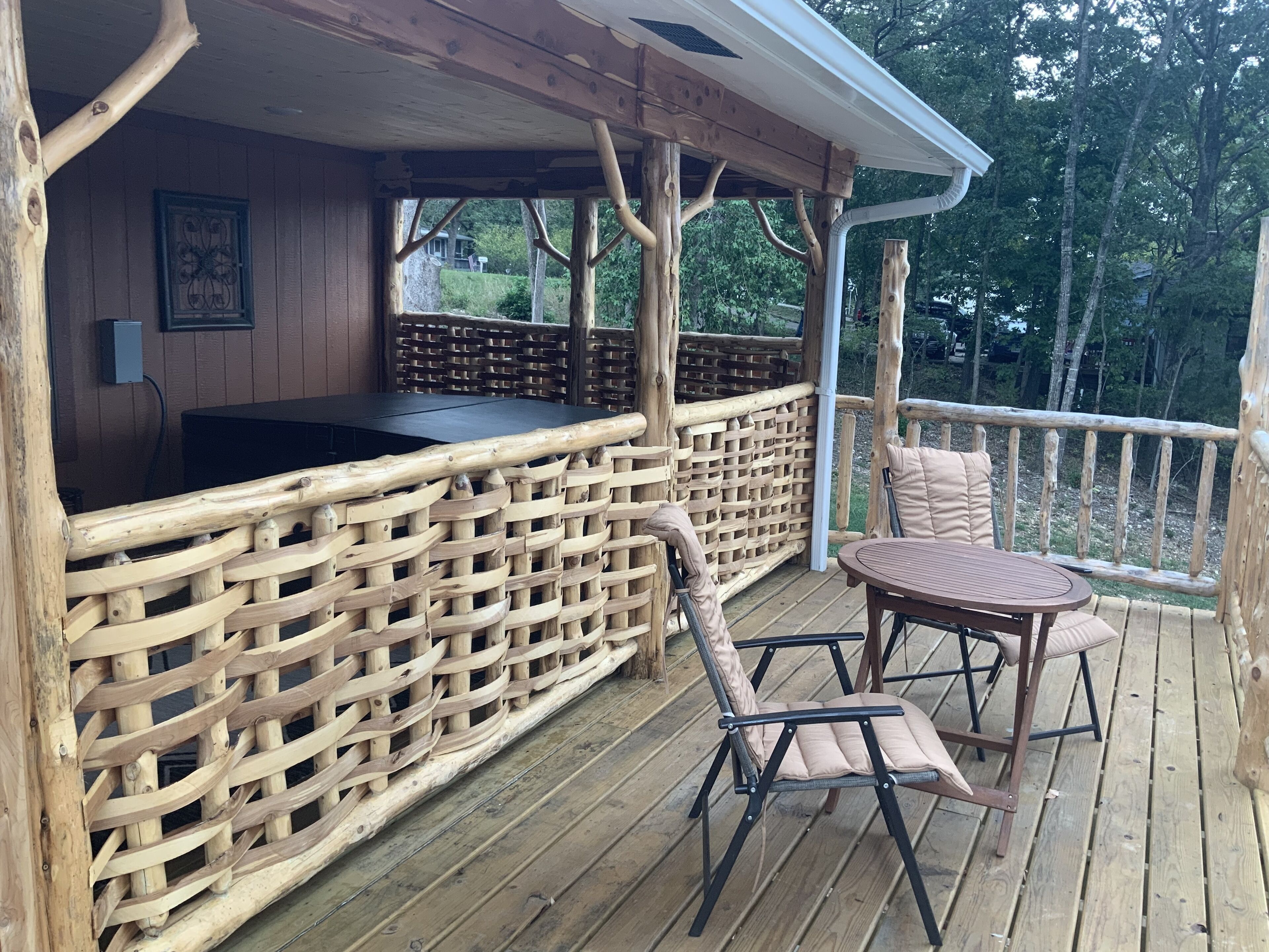 Une terrasse en bois avec un coin bar, des meubles en osier et une vue sur les arbres environnants.