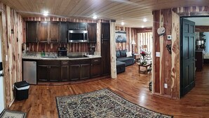 A spacious living area with a wooden floor, a kitchen with dark cabinets and a microwave, and a cozy seating area with a sofa and a coffee table. - Cedar house (Rockaway Beach)