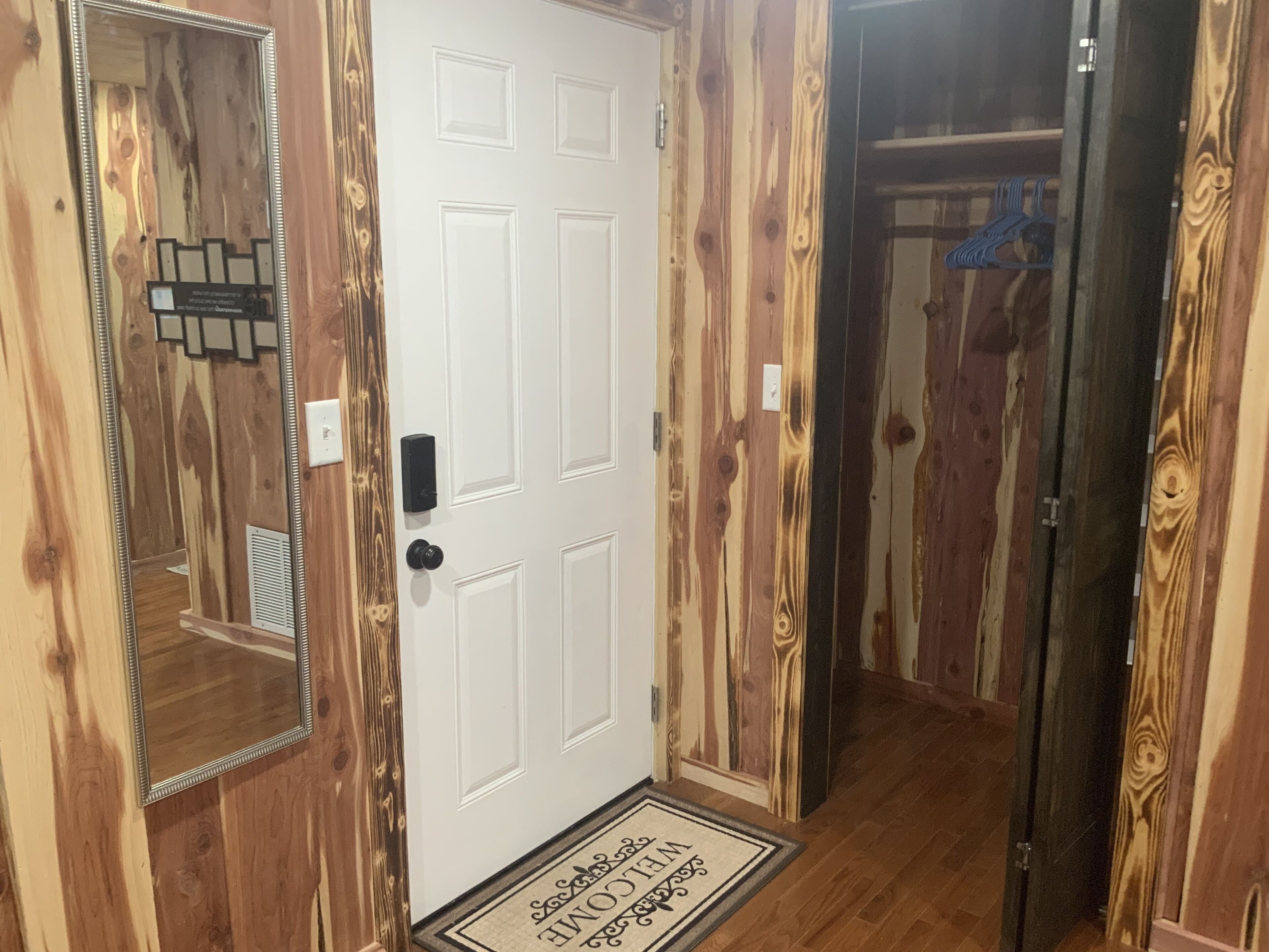 A wooden interior hallway with a white door, a mirror, and a doormat.
