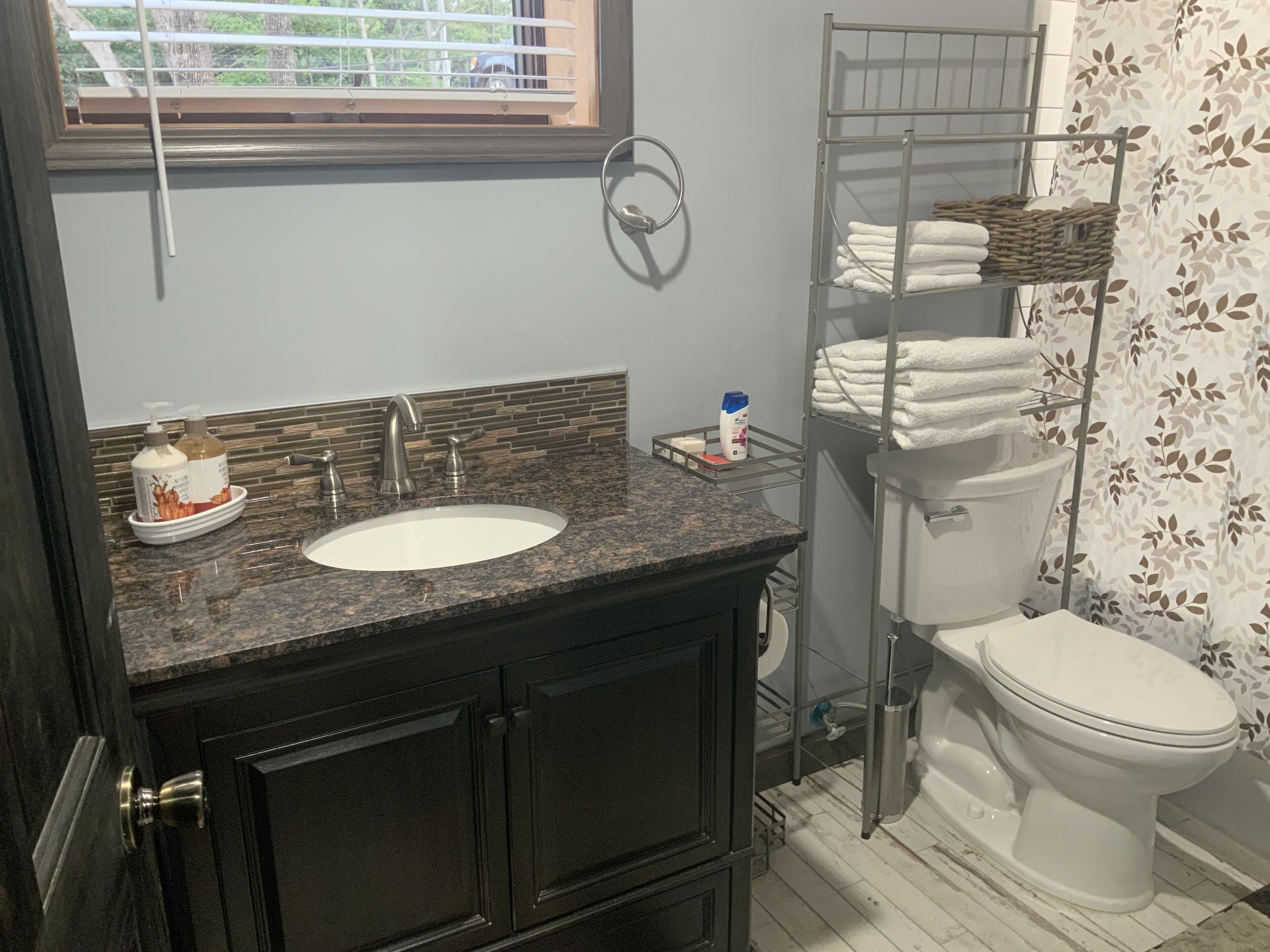 A bathroom with a granite countertop sink, a toilet, and a towel rack with folded towels.