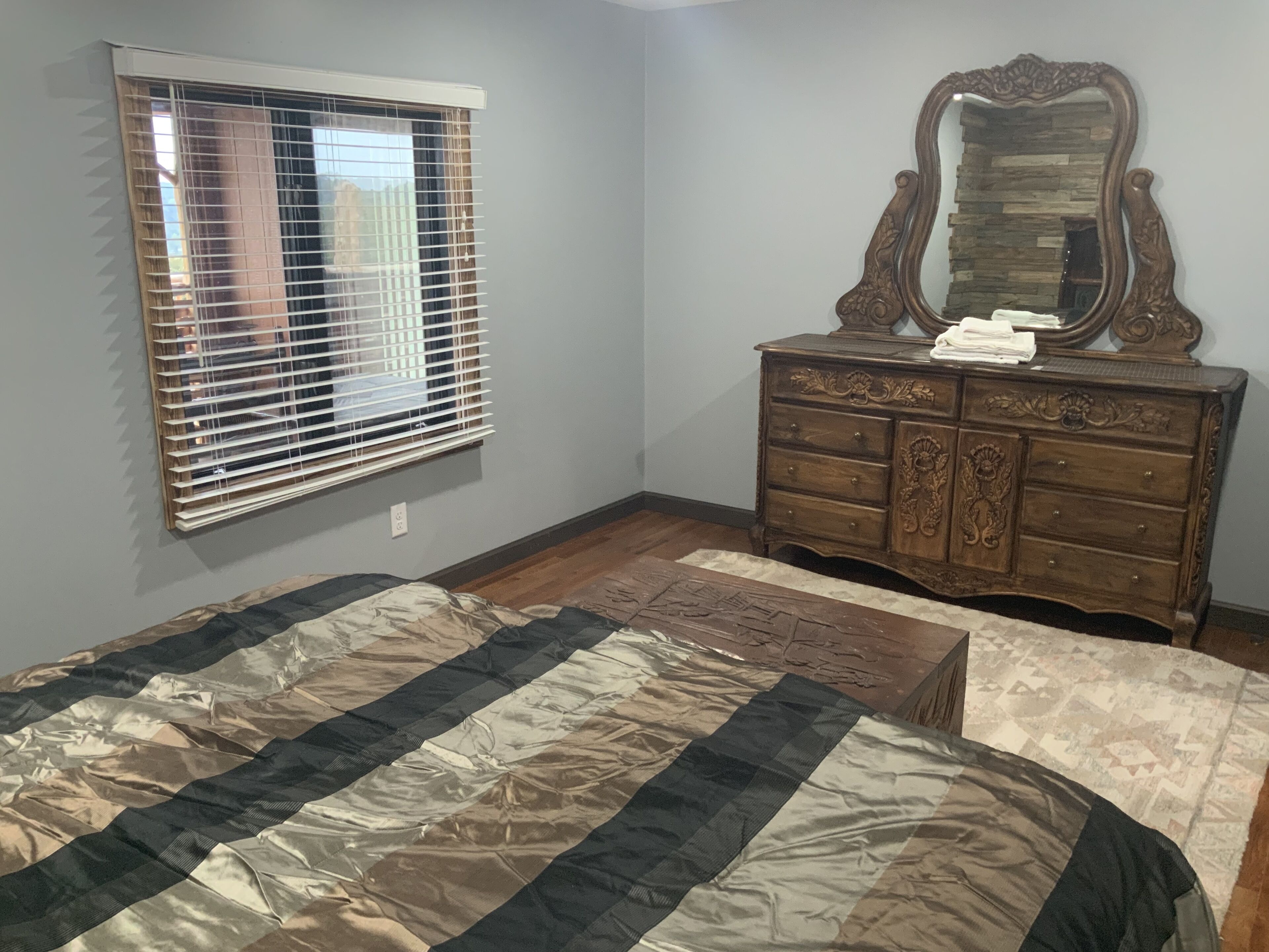 A bedroom with a bed, a dresser, a mirror, and a window with blinds.