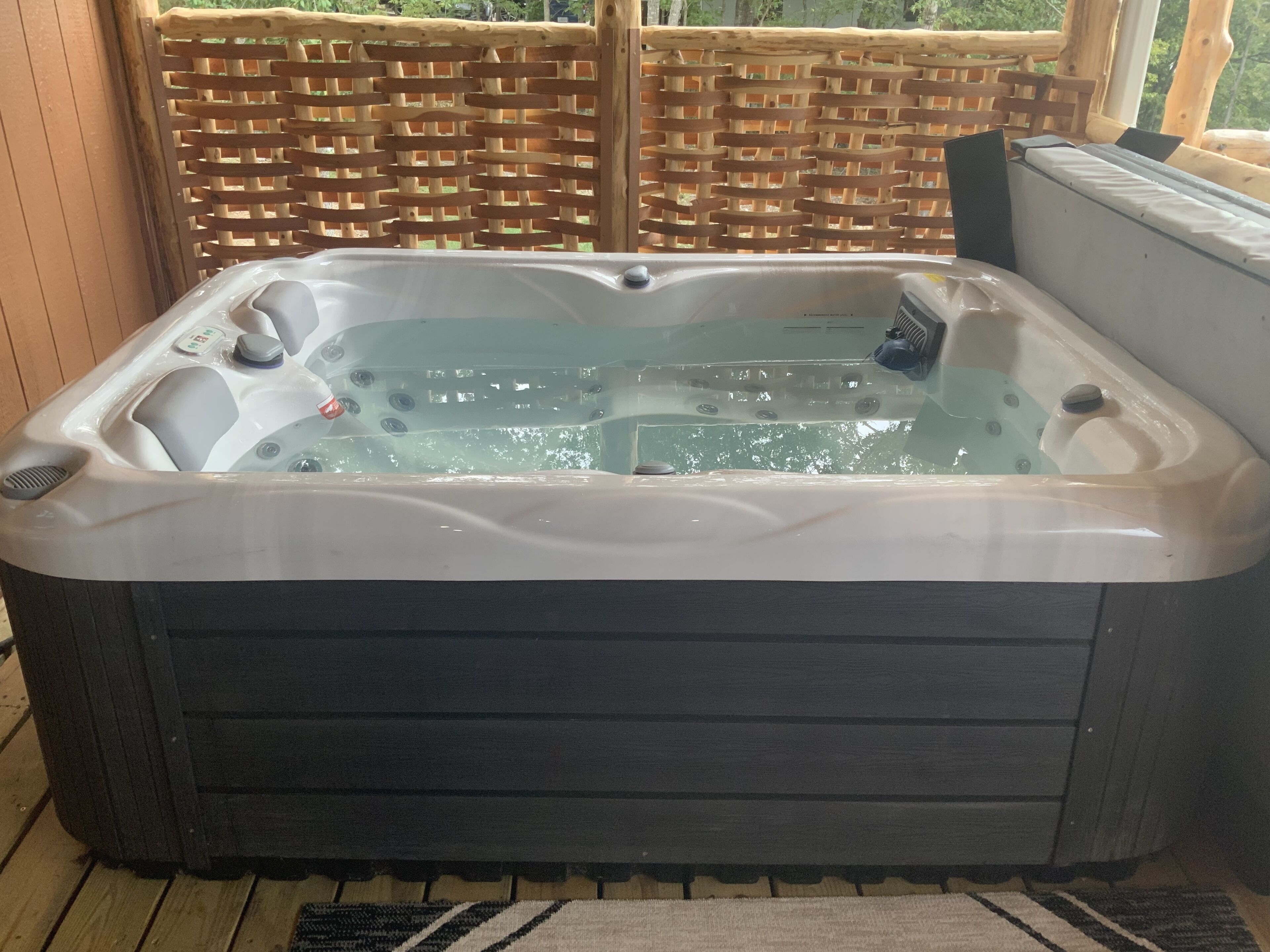 A hot tub with a wooden deck and a woven fence in the background.
