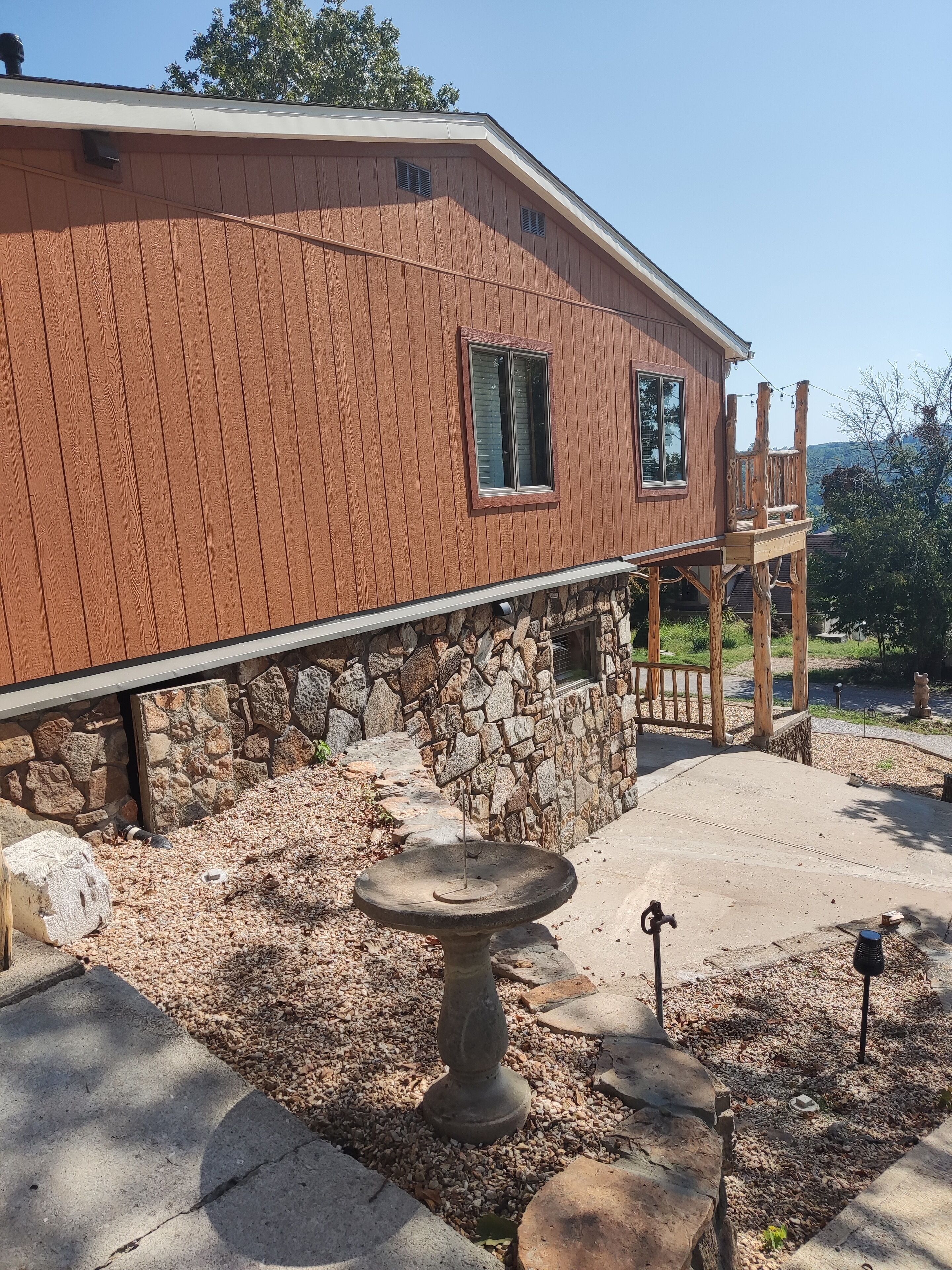 Ein Haus mit Steinfundament, einer Holzterrasse und einem Vogelbad.