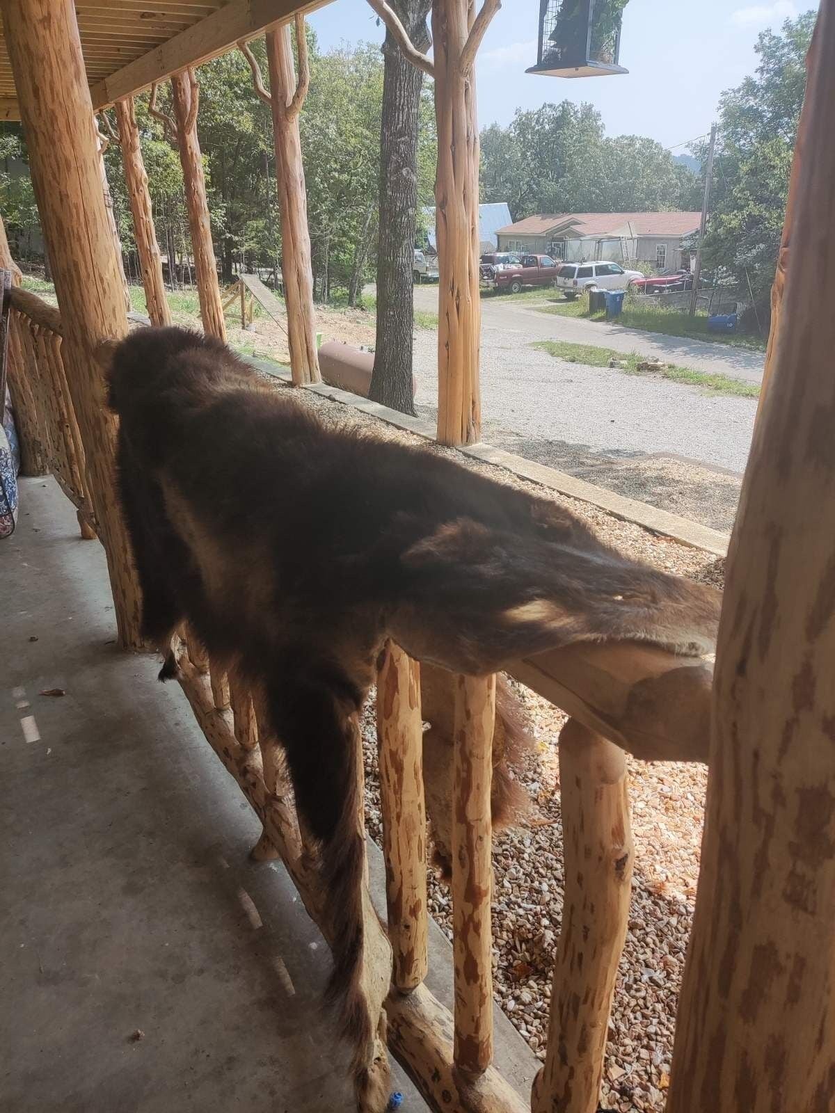 Eine Holzbalkonage mit Betonboden, vermutlich eine Veranda oder ein Balkon, mit Blick auf eine Straße mit parkenden Autos und Häusern.