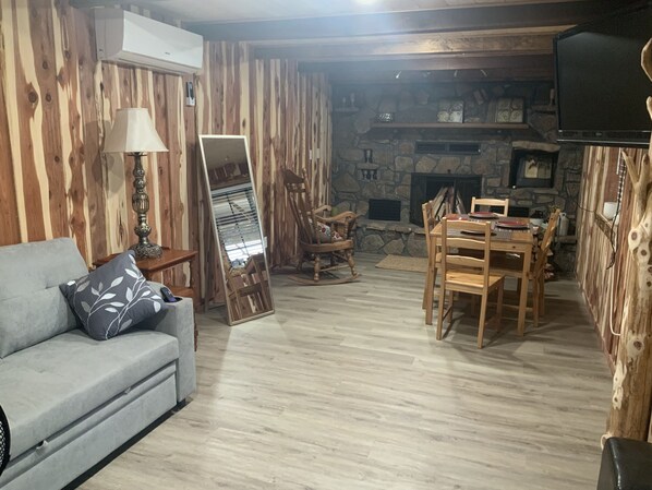 A cozy living room with a stone fireplace, wooden walls, a sofa, and a dining table with chairs. - Cedar house (Rockaway Beach)