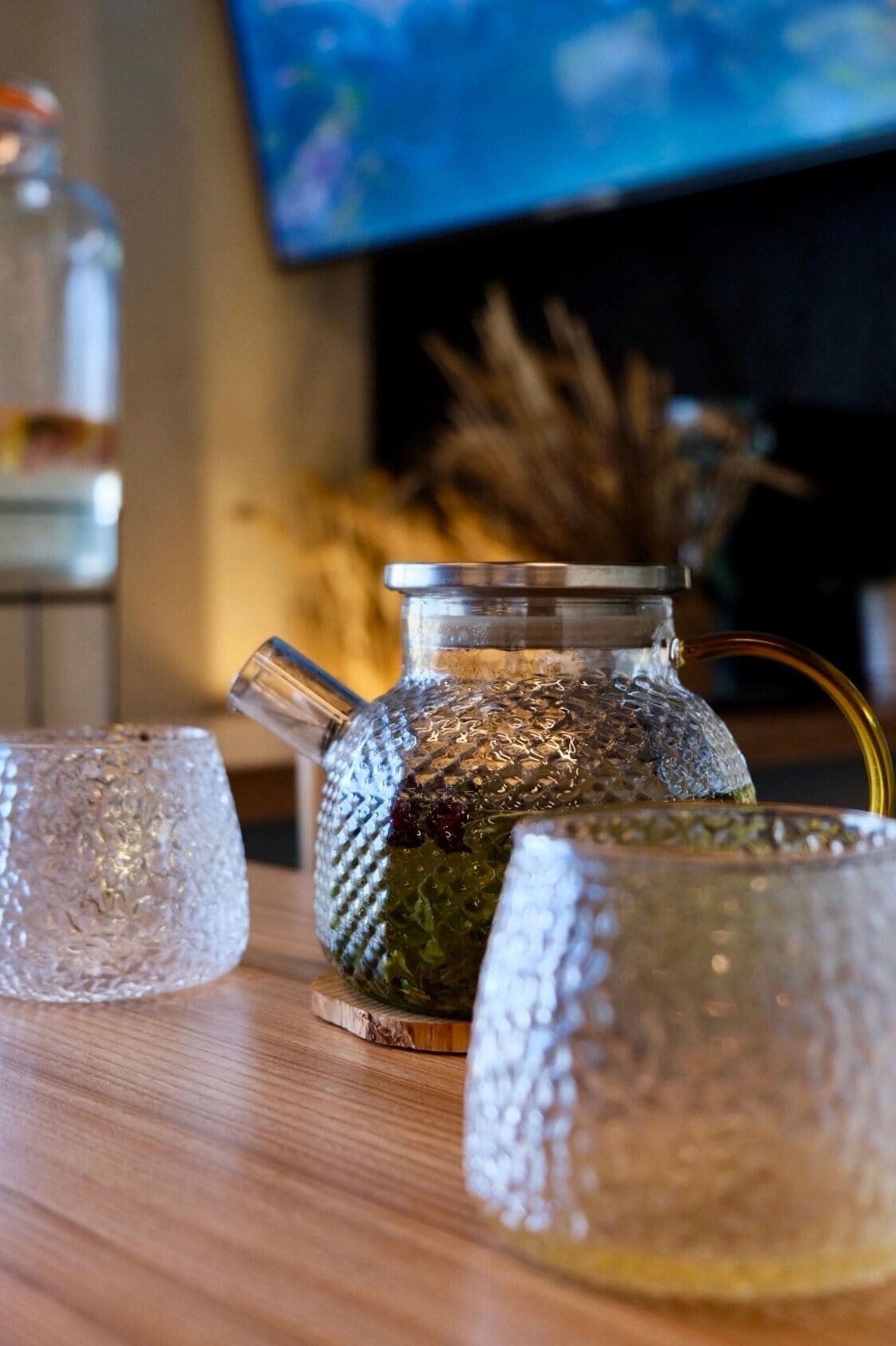 A glass teapot and two glass cups on a wooden table.