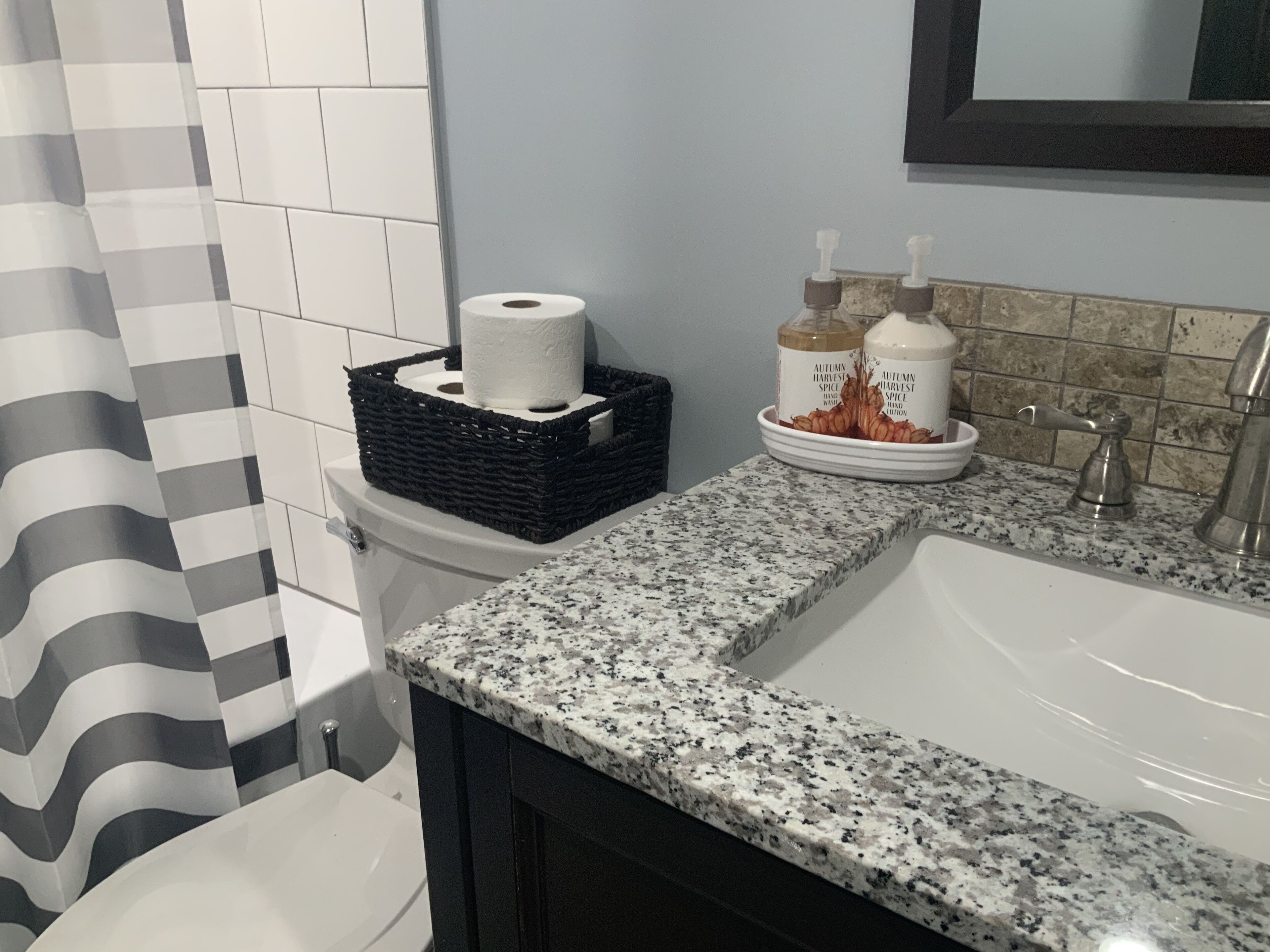 A bathroom with a white sink, a black wicker basket with a roll of toilet paper, and two bottles of hand soap.