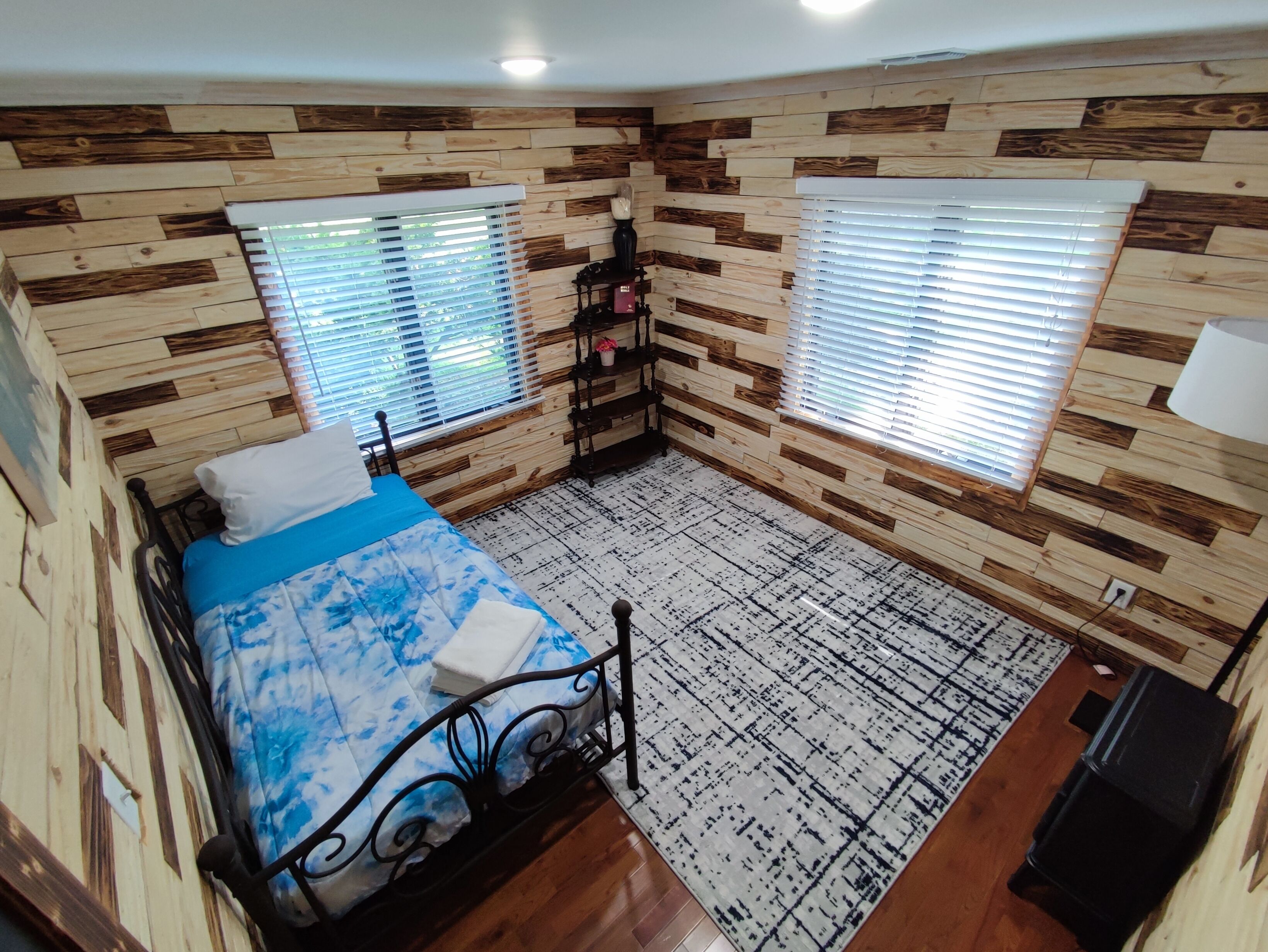 Une chambre à coucher avec un lit, deux fenêtres, une petite étagère et un tapis.