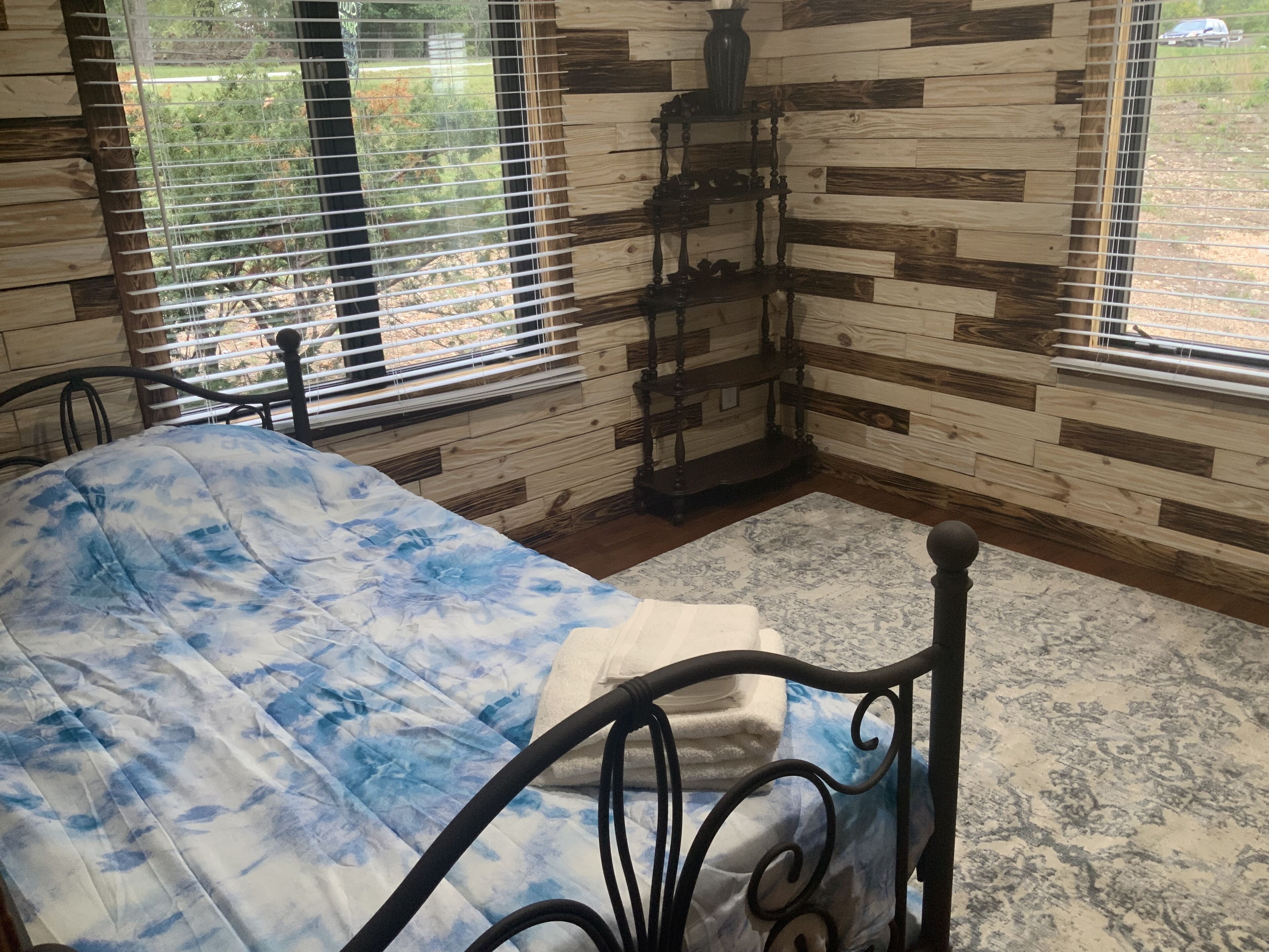 A bedroom with a bed, a window with blinds, a wooden wall, and a small table.