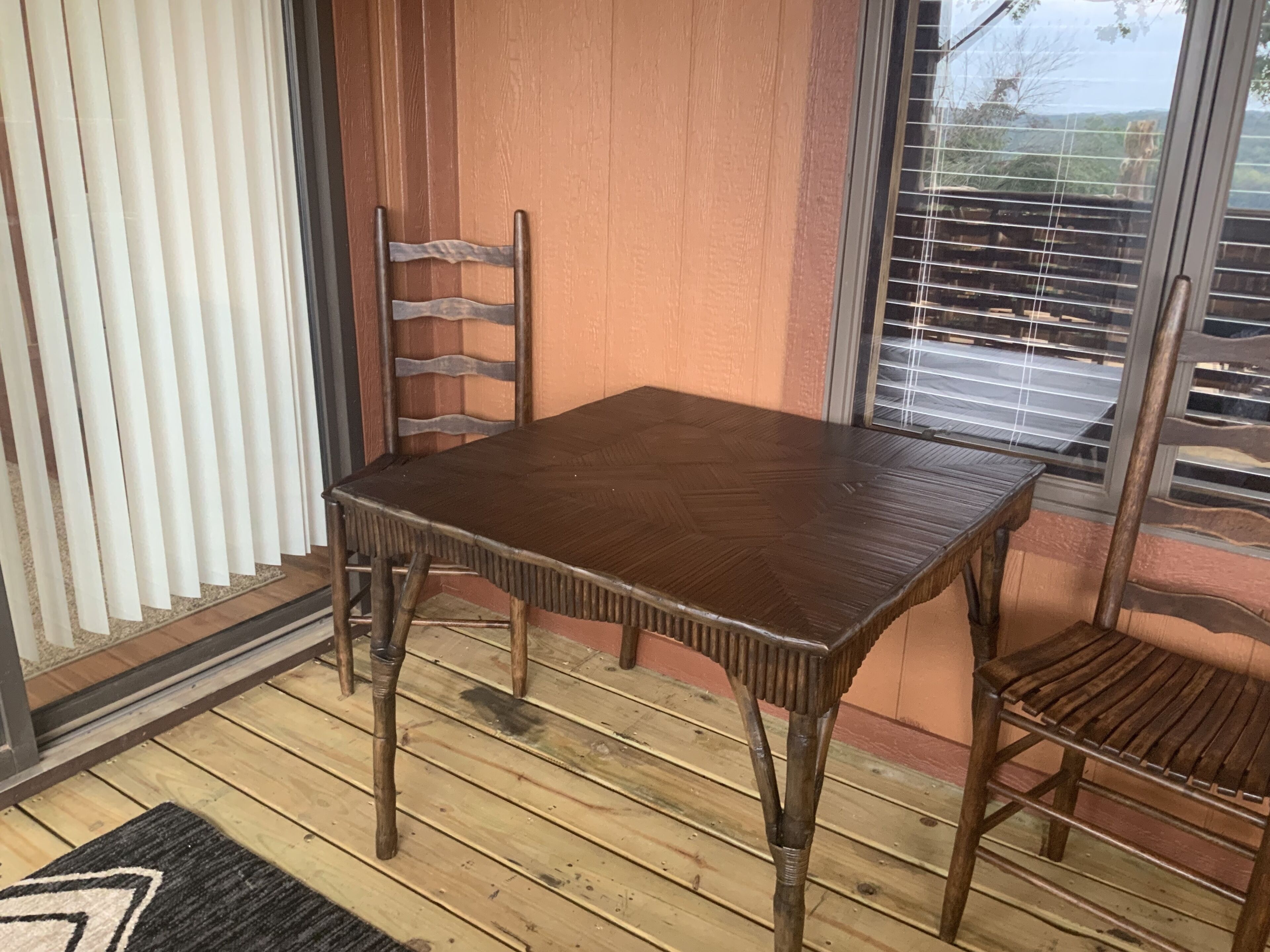 A wooden table and two chairs in a room with a wooden floor, a window with blinds, and a door with vertical blinds.