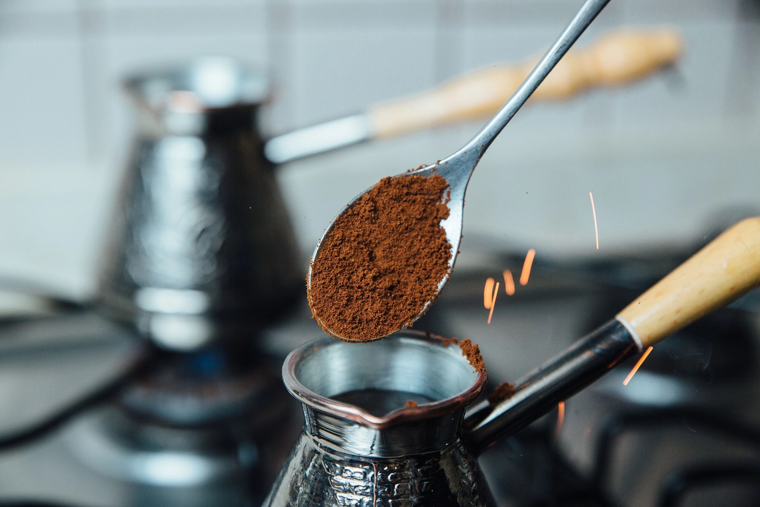 Primer plano de una cuchara de café molido siendo vertida en una cafetera de metal.