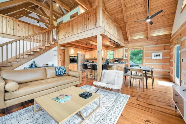 A spacious cabin interior with a wooden staircase, a dining area, a kitchen, and a living room with a sofa and coffee table.