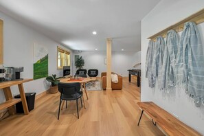 A modern living room with a wooden coffee table, two black chairs, a sofa, a foosball table, and a wall-mounted drying rack.