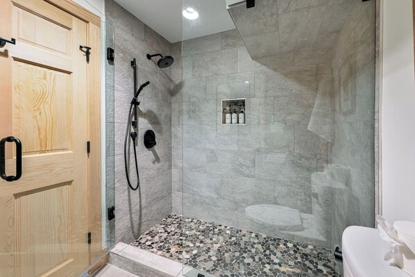 A shower with a handheld showerhead and a wall-mounted one, a tiled floor, and a wooden door.