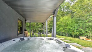 Ein Whirlpool unter einem Vordach mit Blick auf einen Garten und Gartenmöbel.