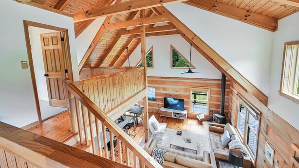 Ein geräumiges Loft mit hoher Decke, Holzbalken, einem Fernseher, einer Sitzecke und einem Balkon mit Aussicht.