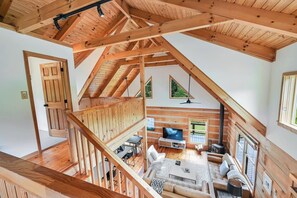 A spacious loft with a high ceiling, wooden beams, a TV, seating area, and a balcony with a view.