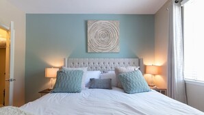 Ein Schlafzimmer mit einer gepolsterten Kopfteil, einem großen runden Kunstwerk über dem Bett und zwei Nachttischlampen.