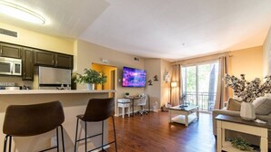 Eine moderne Wohnung mit Küche, Essbereich und Wohnzimmer. Sie verfügt über einen Flachbildfernseher, einen Esstisch mit Stühlen, ein Sofa und einen Couchtisch.