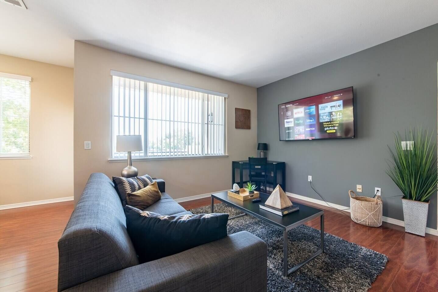 Una sala de estar moderna con un sofá gris, una mesa de centro y un televisor montado en la pared.