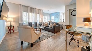 A modern living room with a sofa, armchair, and coffee table, a dining area with a glass table, and a kitchen in the background. - Sky Luxury 2BDRM Suite | Deluxe Living Cali (Valencia)