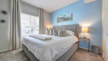 A bedroom with a bed, a nightstand, a lamp, a mirror, and a window with curtains.