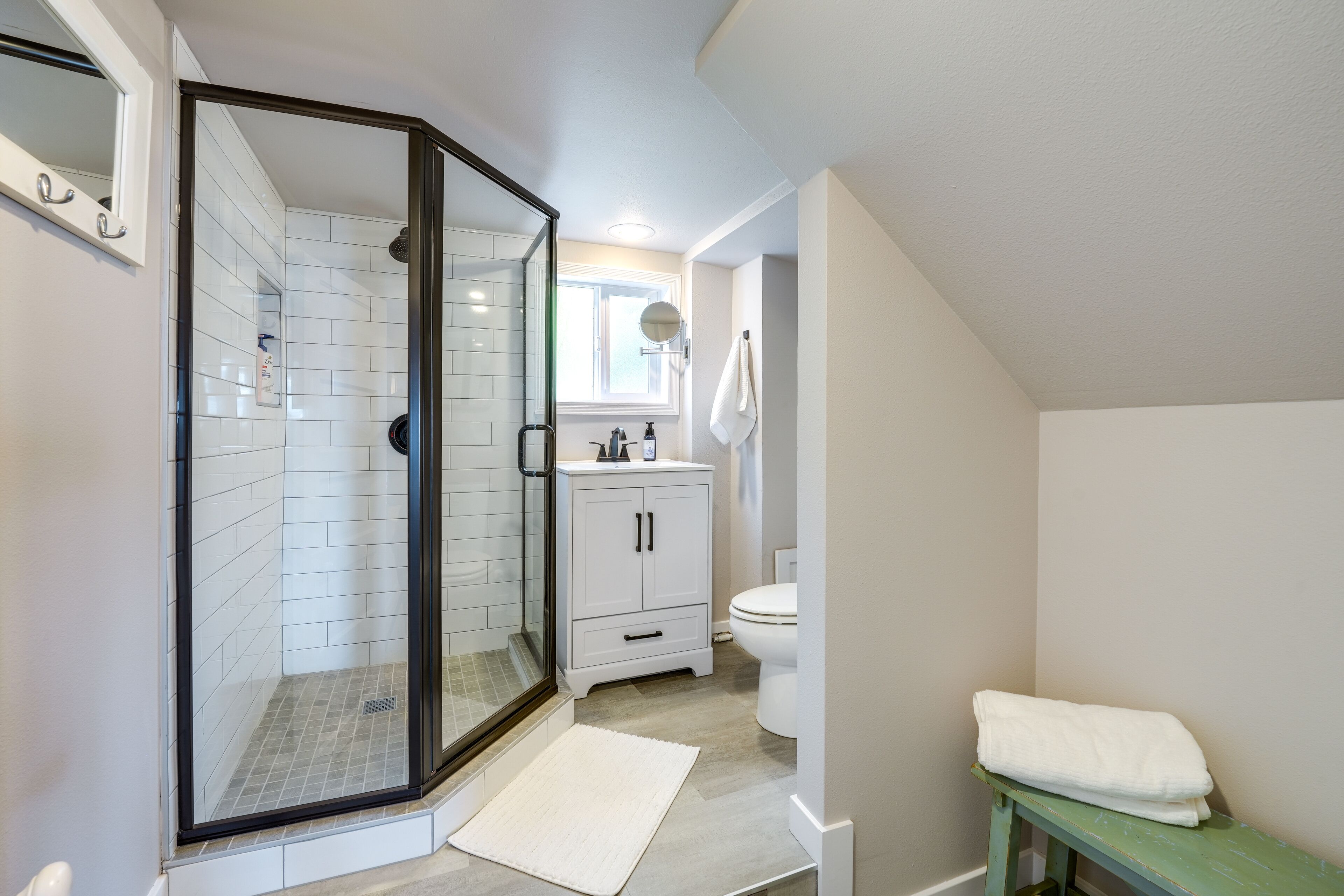 Une salle de bain moderne avec une douche à parois de verre, des toilettes blanches et un petit banc sur lequel est posée une serviette.