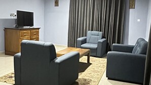 A living room with a flat-screen TV, two sofas, a coffee table, and a ceiling fan. - ACHIE SUITES (Accra)