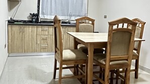 A dining area with a wooden table and chairs, a ceiling fan, and a kitchen in the background. - ACHIE SUITES (Accra)