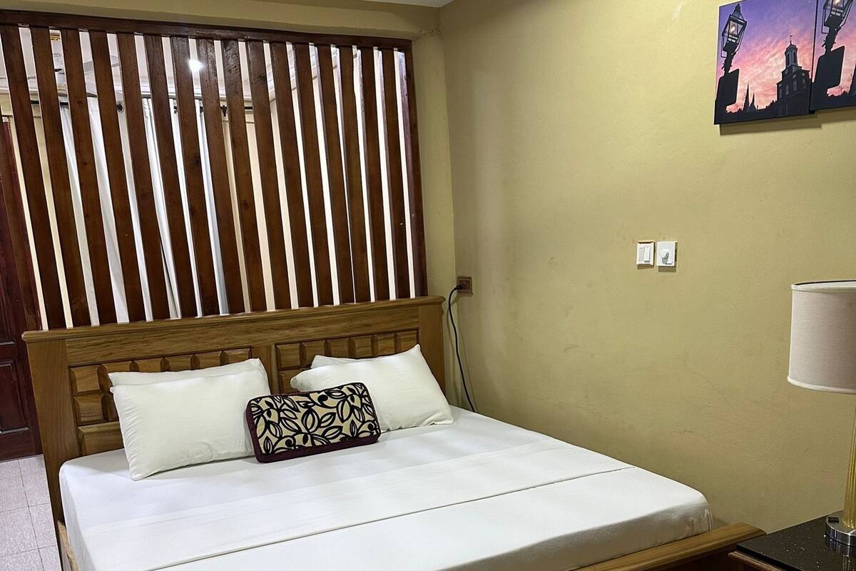 A neatly made bed with a wooden headboard, a bedside table with a lamp, and a wall-mounted painting.