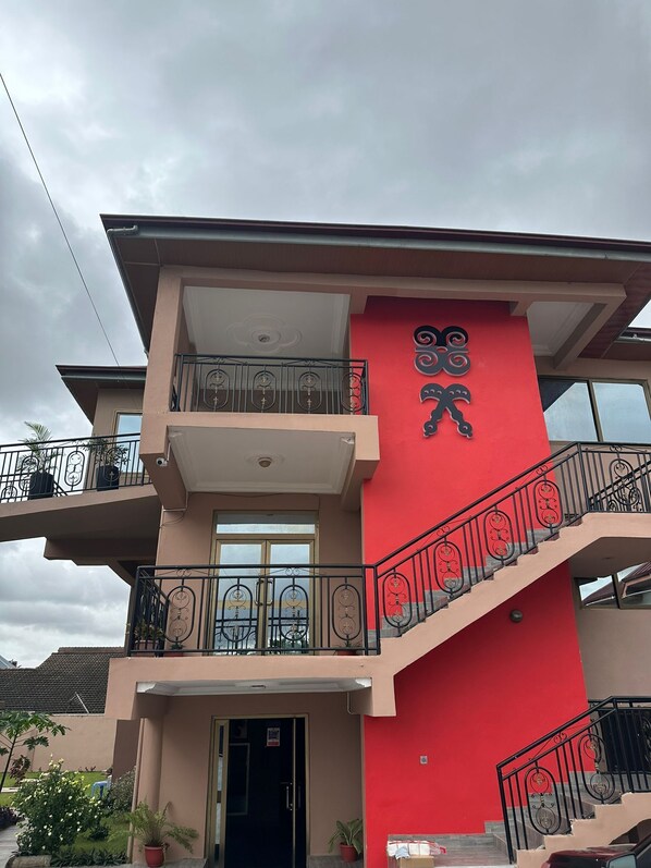 Un immeuble de deux étages avec une façade rouge, un balcon orné de balustrades décoratives et un escalier doté de balustres travaillées.