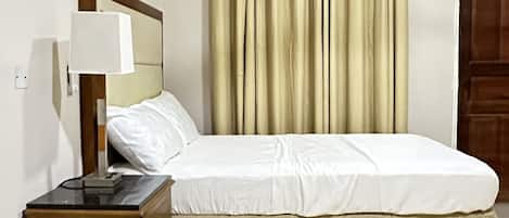 A bedroom with a bed, bedside table, lamp, and curtains.