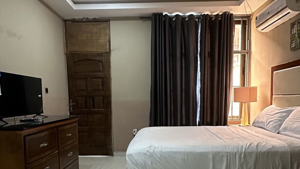 A bedroom with a bed, a ceiling fan, a TV on a dresser, and an air conditioning unit. - ACHIE SUITES (Accra)