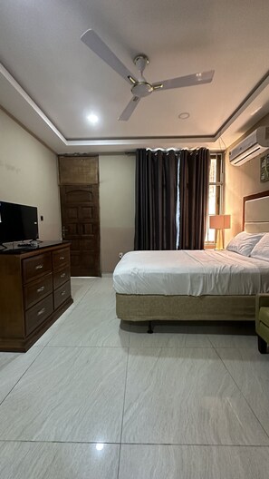 A bedroom with a bed, a ceiling fan, a TV on a dresser, and an air conditioning unit. - ACHIE SUITES (Accra)