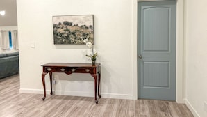 A room with a wooden console table, a framed landscape painting, a light blue door, and a window with curtains. - The Modern Cottage in Rural Lake Stevens (Lake Stevens)
