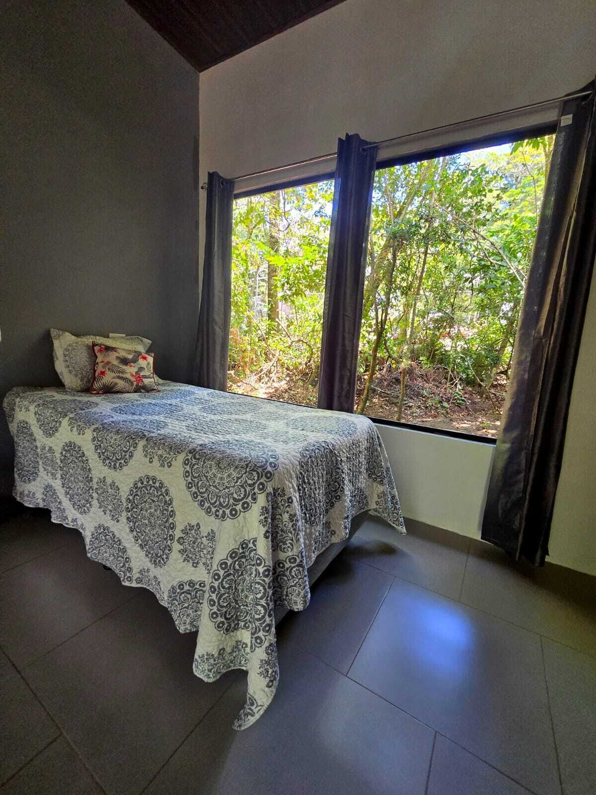 A bedroom with a bed, curtains, and a view of trees.