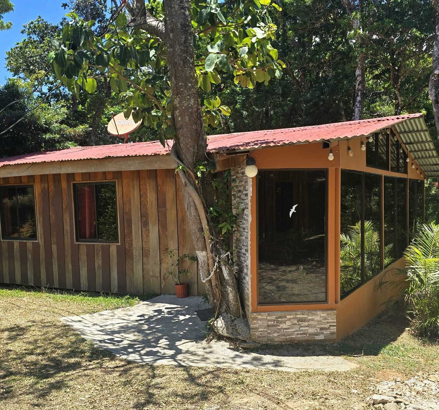 Una cabaña de madera con techo rojo, cerramiento de vidrio y una antena parabólica.