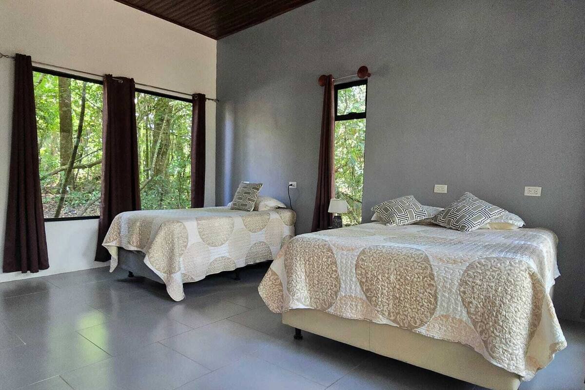 A bedroom with two beds, large windows, and a tiled floor.