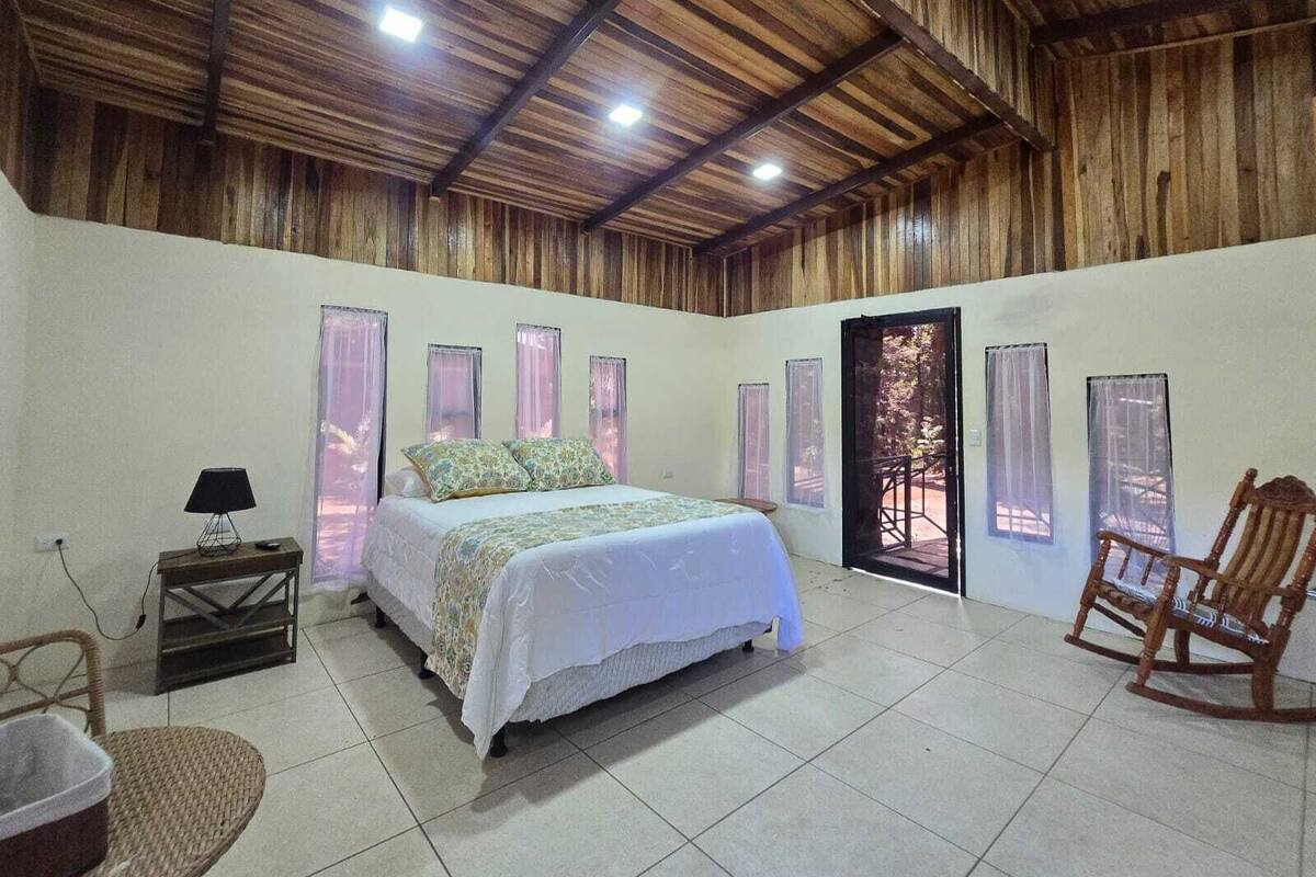 A bedroom with a bed, a chair, a lamp, and a view through a door.