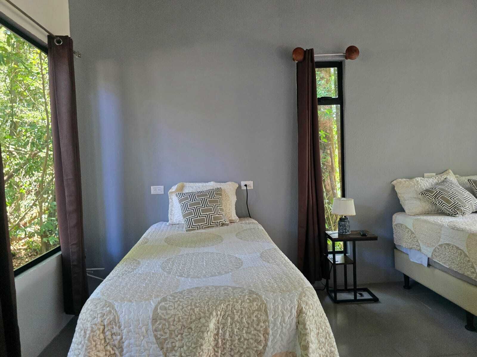 A room with a bed, a bedside table with a lamp, and a window with curtains.
