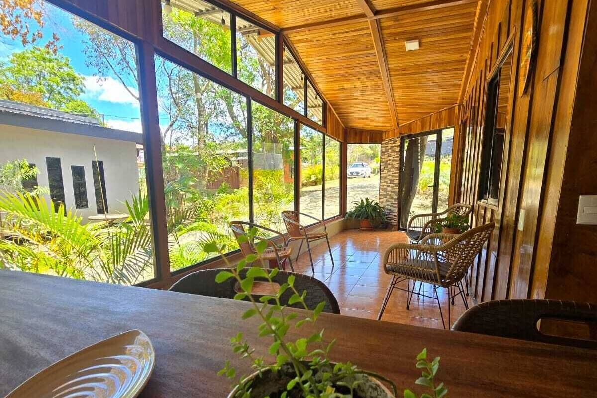 A spacious room with large windows, wooden ceiling, and a dining area with chairs and a table.