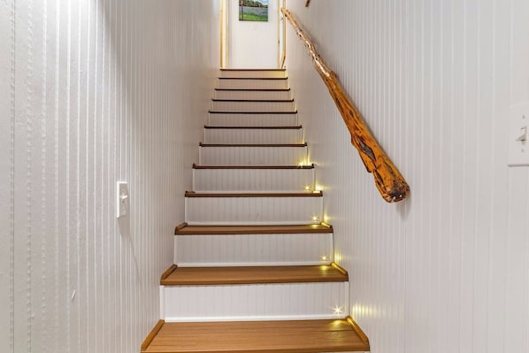Eine Treppe mit Holzstufen und einer Handlauf, die zu einer Zwischenebene mit Lichtschalter und einem gerahmten Bild führt.