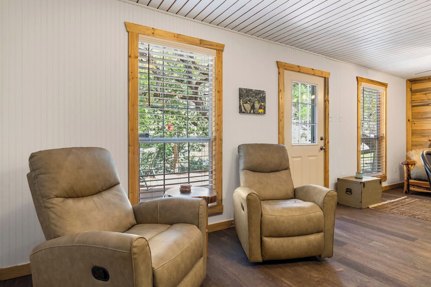 Une pièce avec deux fauteuils inclinables en cuir, une porte en bois et de grandes fenêtres équipées de stores.